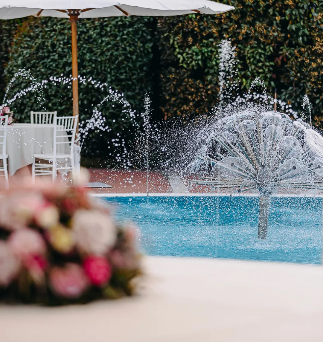 La piscina con la fontana e i tavoli sotto l'ombrellone