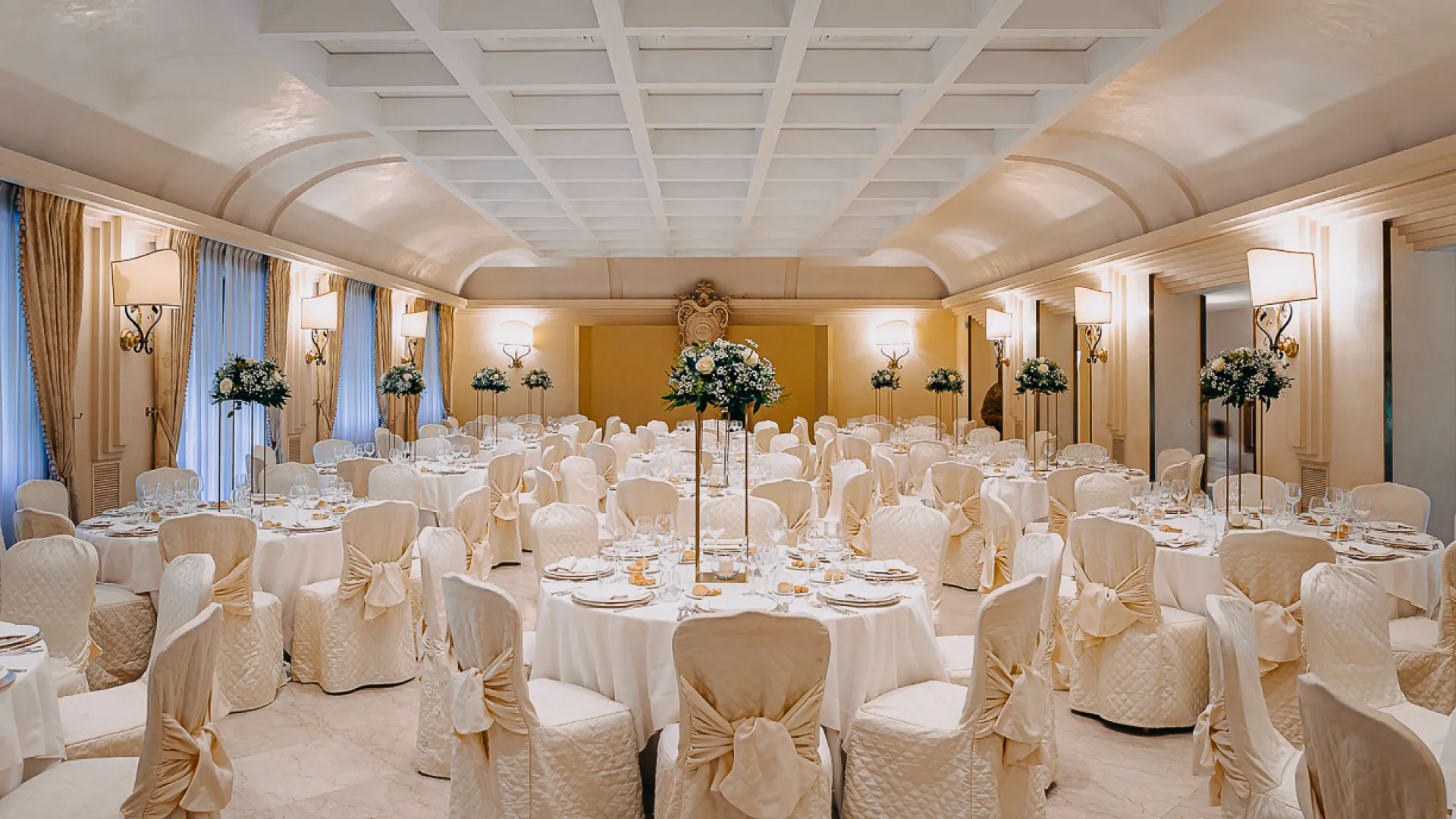 Sala interna con tavoli rotondi apparecchiati e composizioni floreali